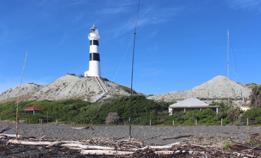Cape Campbell lighthouse with radio aerial poles in the foreground along the high tide line.