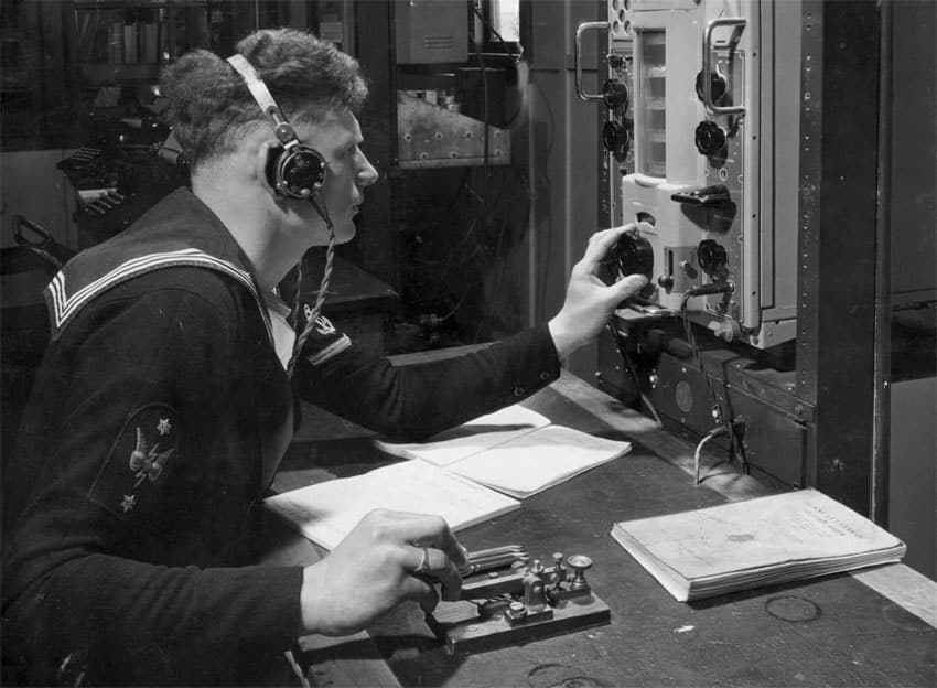 Radio operator at HMNZS Irirangi, sending on a straight key while tuning a Murphy B40 receiver