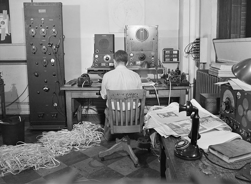 Radio listening room, New York Times, 1942. A man is seated in front of HRO receivers, with piles of paper tape from perforators on the floor.