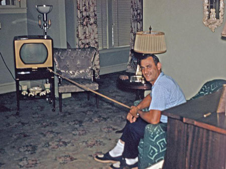Photo from 1950s shows many in living room with long stick to change channels on TV set