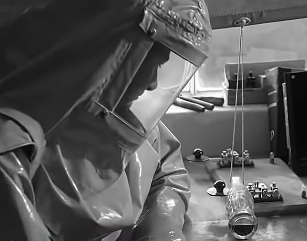 Man in radiation suit looking at coke bottle caught in strike on window blind and tapping randomly on a morse key, from the film On the Beach