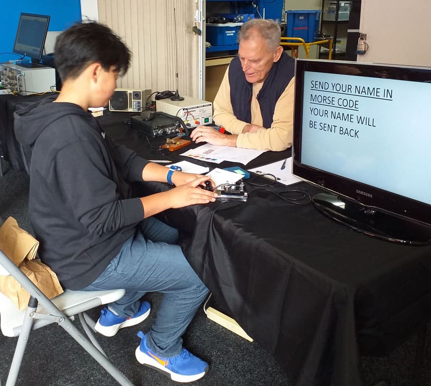 Young boy practising Morse Code on a straight key under the watchful eye of an experienced radio amateur