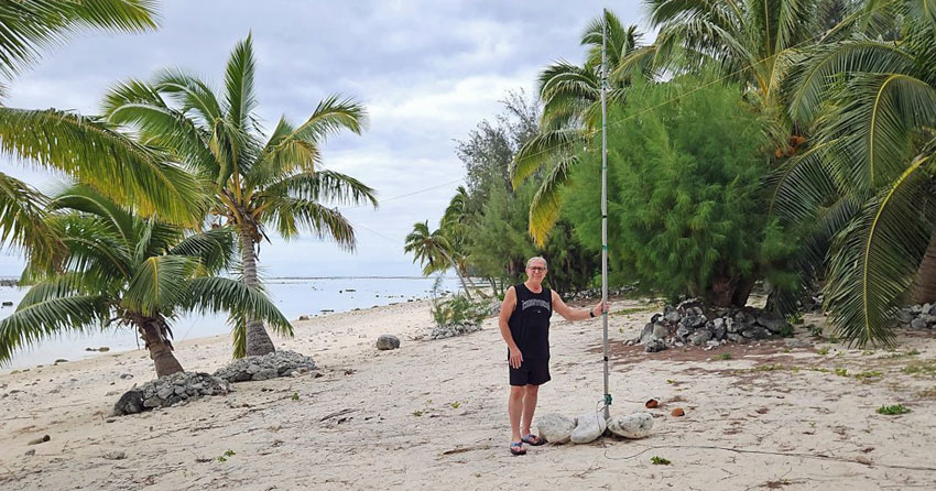 Steve E51KEE holding antenna pole on beach at Rarotonga, 2024