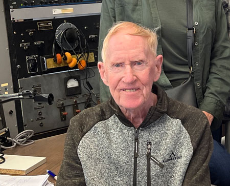 Elderly man seated in front of vintage radio console