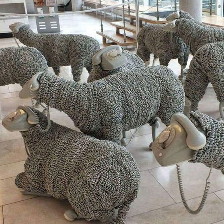 Art installation with flock of sheep with old telephone sets for heads and bodies covered in curly cord
