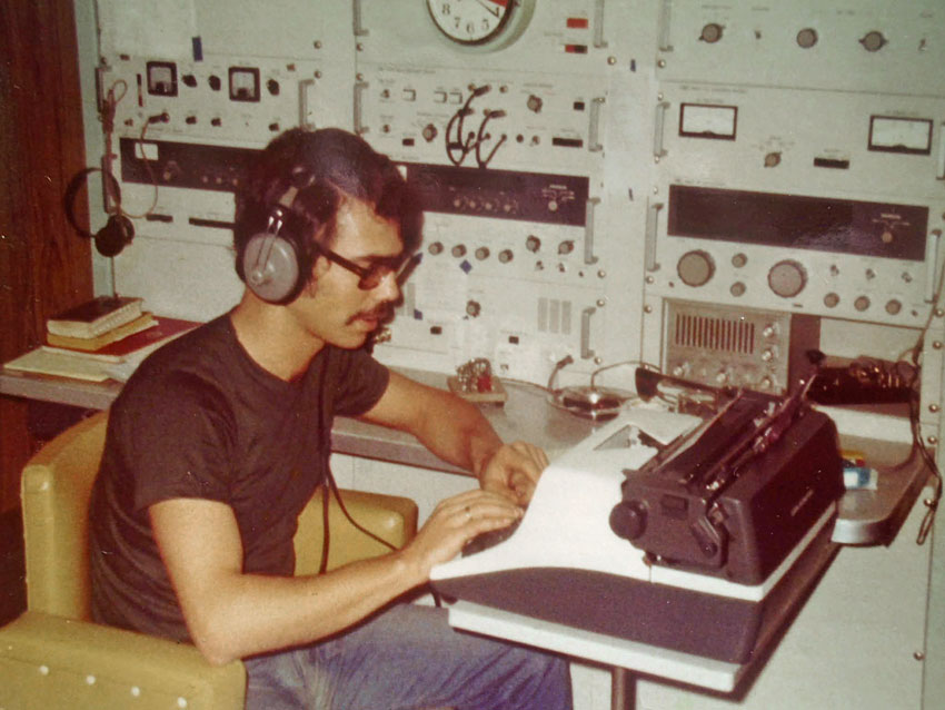 Ship radio officer, not in uniform, wearing headphones and typing